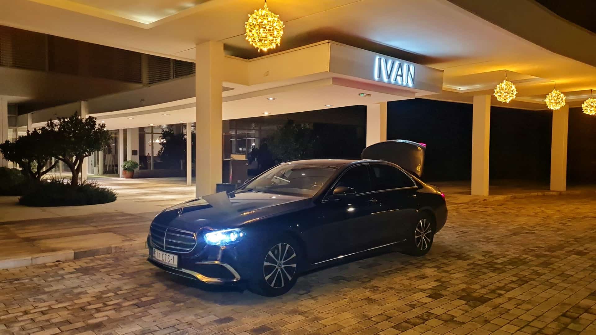 Amadria Park - Taxi Sibenik Cipollina - Hotel transfer: premium sedan at the illuminated IVAN hotel entrance, trunk open ready for guest luggage